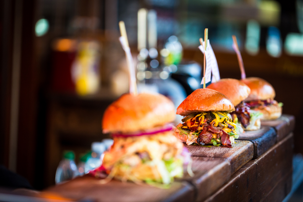 close up of three burgers on a wooden counter 